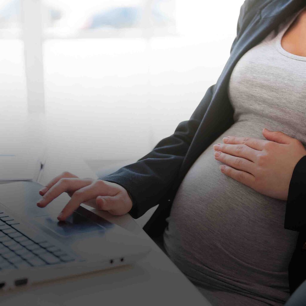 Foto de uma mulher grávida mexendo no computador, ilustrando o tema do texto sobre direitos das gestantes no ambiente de trabalho